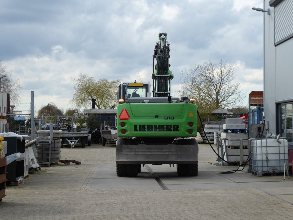 Rear view of a green Liebherr excavator on an outdoor industrial site under cloudy skies.